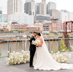A bride and groom pose with their foreheads touching in front of baby's breath ground arch on the riverfront patio {{brizy_dc_image_alt imageSrc=