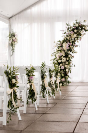 Ceremony Setup on Rooftop with White Drapery and White Seating with Floral Arrangements of Purple and Green {{brizy_dc_image_alt imageSrc=