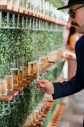 Guest grabbing champagne from greenery wall during reception {{brizy_dc_image_alt imageSrc=