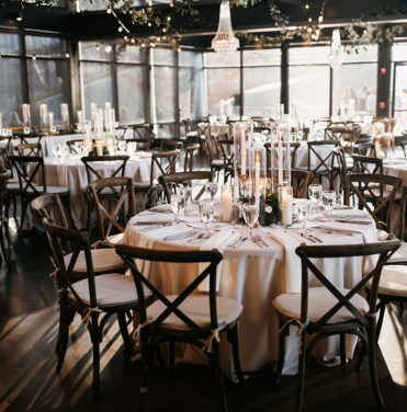 Cassidy-Darius Wedding Reception in the Cumberland Space Round wedding tables with dark brown chairs, white linens, candle centerpieces, and crystal chandeliers in the Cumberland space with natural light shining in