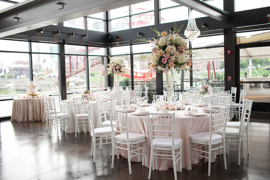 Glam pink wedding reception setup with pale pink table linens, white chairs, and large elevated floral centerpieces in class vases at The Bridge Building, downtown Nashville wedding venue {{brizy_dc_image_alt imageSrc=