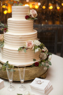 Four-tier white textured wedding cake with red and pink rose decor for romantic winter wedding at The Bridge Building, downtown Nashville wedding venue {{brizy_dc_image_alt imageSrc=