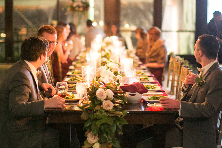 Guests seated at wedding reception head table with magnolia leaves for table runner and red napkins for romantic winter wedding at The Bridge Building, downtown Nashville wedding venue {{brizy_dc_image_alt imageSrc=