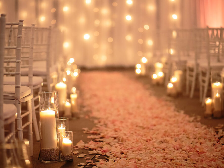 A close-up of pink rose petals creating an aisle to the altar, surrounded by candle aisle markers for rose gold New Year's Eve wedding at the Bridge Building, a downtown Nashville wedding venue {{brizy_dc_image_alt imageSrc=