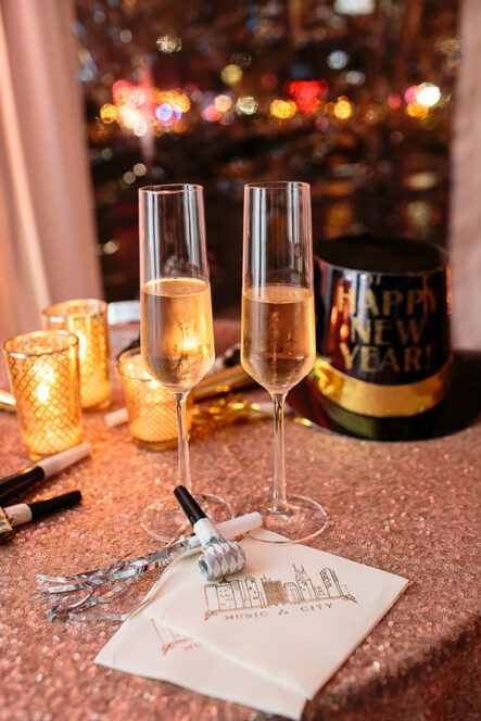 Bride and groom champagne flutes set up on rose gold sequin table linens with happy new year's hat and streamers for New Year's Eve wedding at the Bridge Building, a downtown Nashville wedding venue {{brizy_dc_image_alt imageSrc=