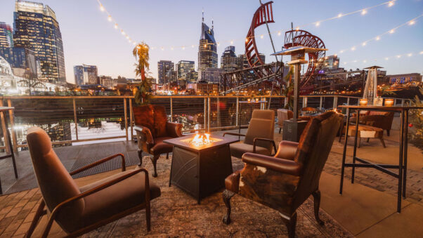 Restaurant-Group Corporate Party Reception on the Riverfront with Lounge Area Modern western-inspired lounge furniture surrounding a fire pit underneath string lights on the riverfront patio overlooking downtown Nashville at dusk