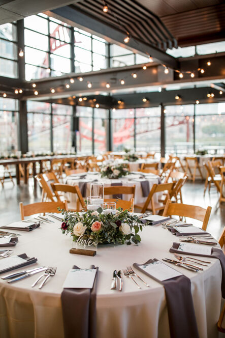 Wedding reception table for romantic natural wedding with ivory linens, brown satin napkins, and greenery centerpiece with wooden and acrylic table numbers