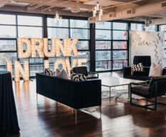 A wedding reception set with a black and white themed lounge area featuring a textured photo booth wall, large marquee letter lights that say 