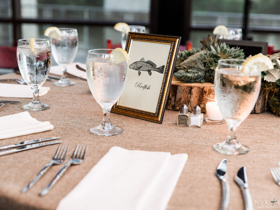 Table decor with fish-themed table numbers, succulents, and slice of wood tree centerpiece for nautical themed rehearsal dinner {{brizy_dc_image_alt imageSrc=