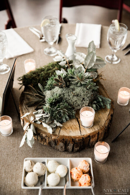 Table decor centerpiece with succulents, moss, and small votive candles on a slice of wooden tree for nautical themed rehearsal dinner {{brizy_dc_image_alt imageSrc=